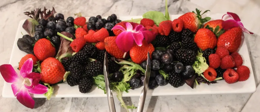 A long platter of strawberries, blackberries and blueberries garnished with orchids