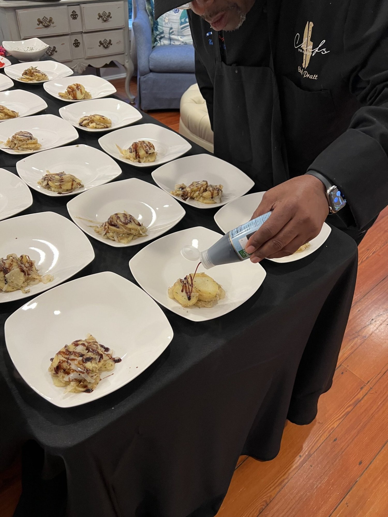 Chef Pratt drizzling sauce over a row of plated courses on a black-draped table
