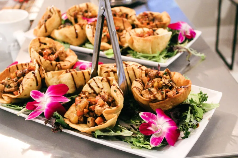Crisp taco cups filled with a savory filling on a platter of greens and pink orchids